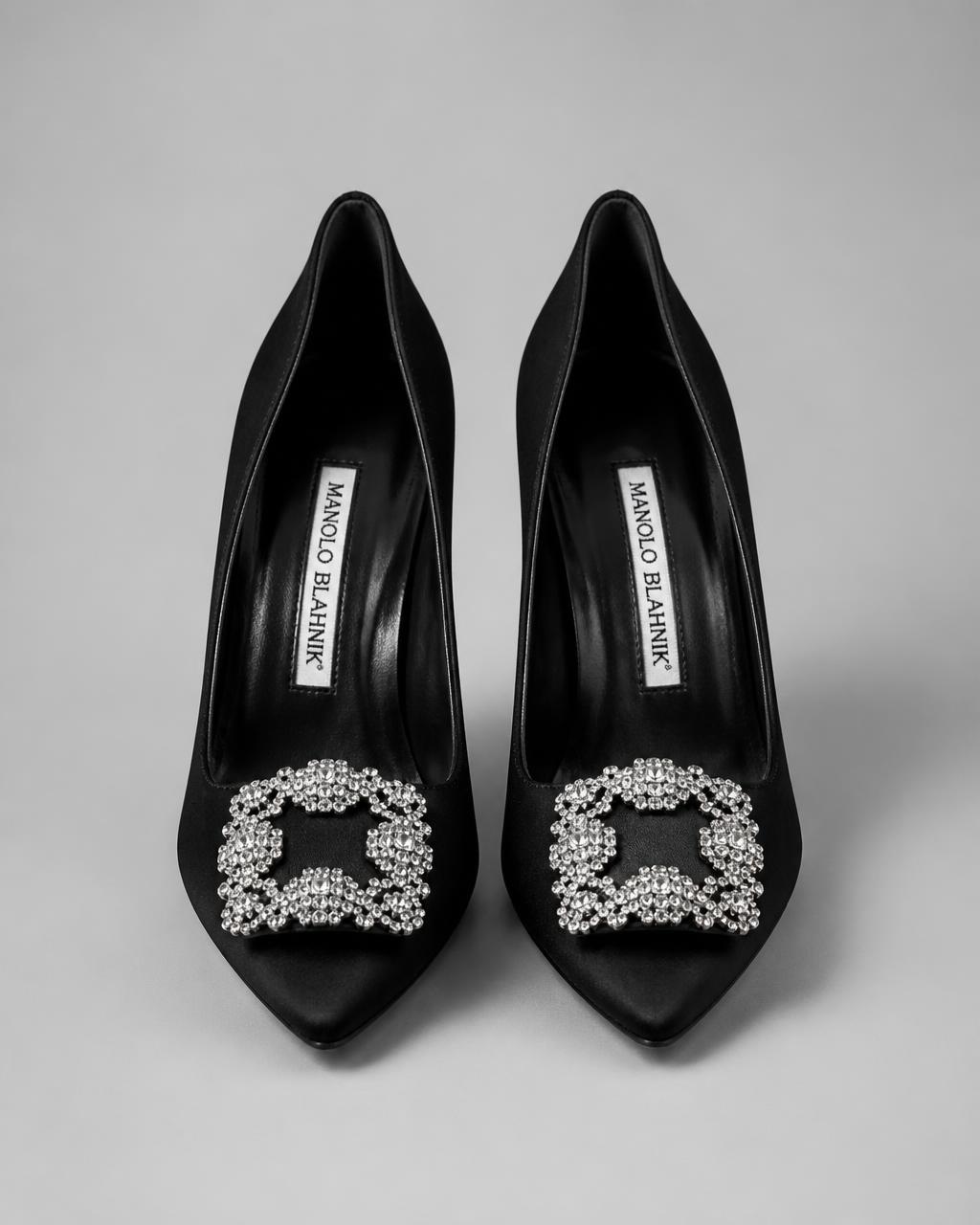 Black satin pumps with crystal buckle on grey studio backdrop